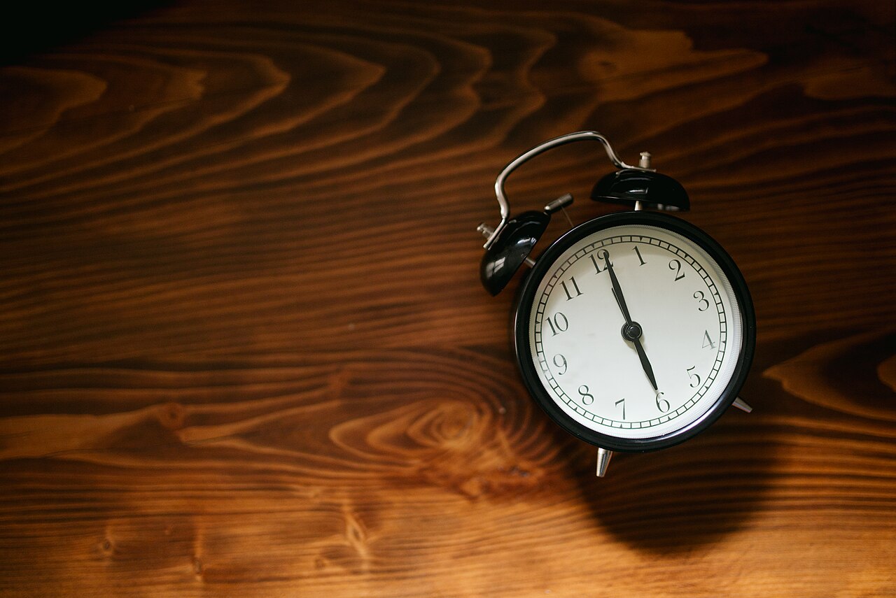 Black alarm clock on wooden surface shows time in simple design