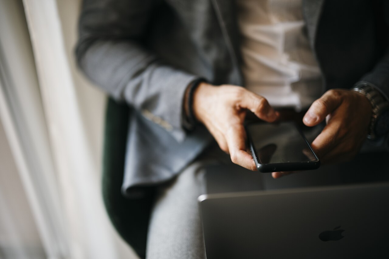 Businessman holds smartphone while sitting with a laptop closeup