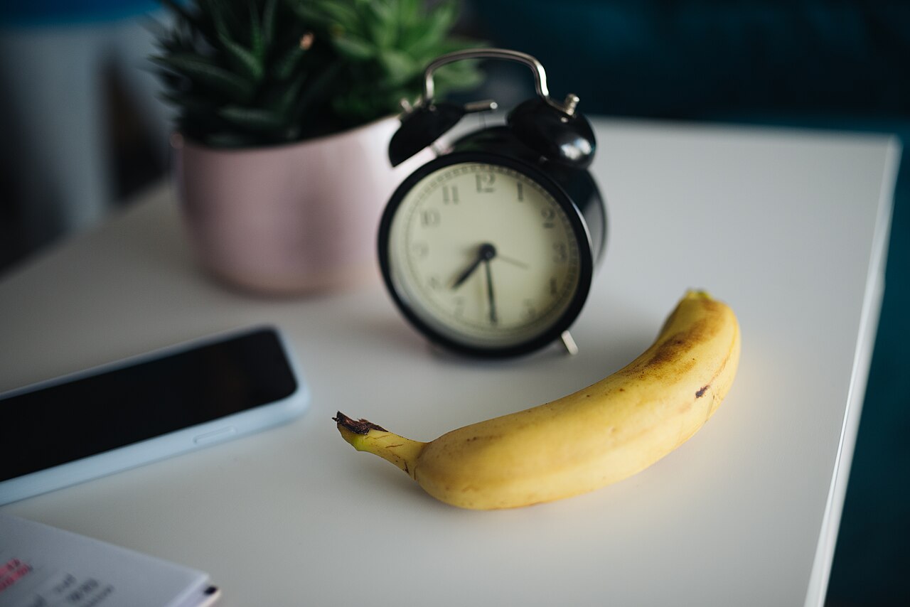 Clock and banana on a table with a smartphone and a plant