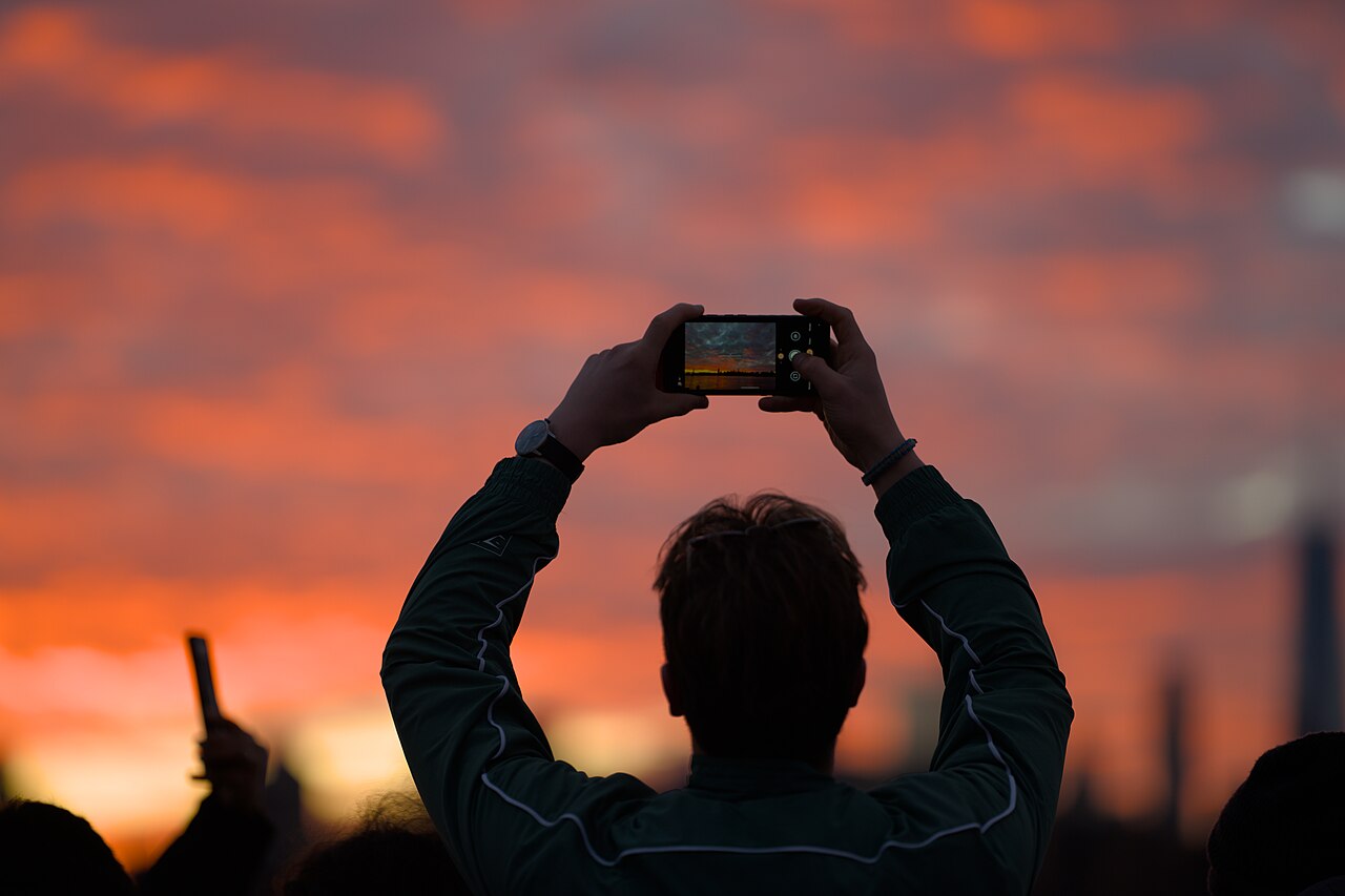 Person capturing a sunset on a smartphone