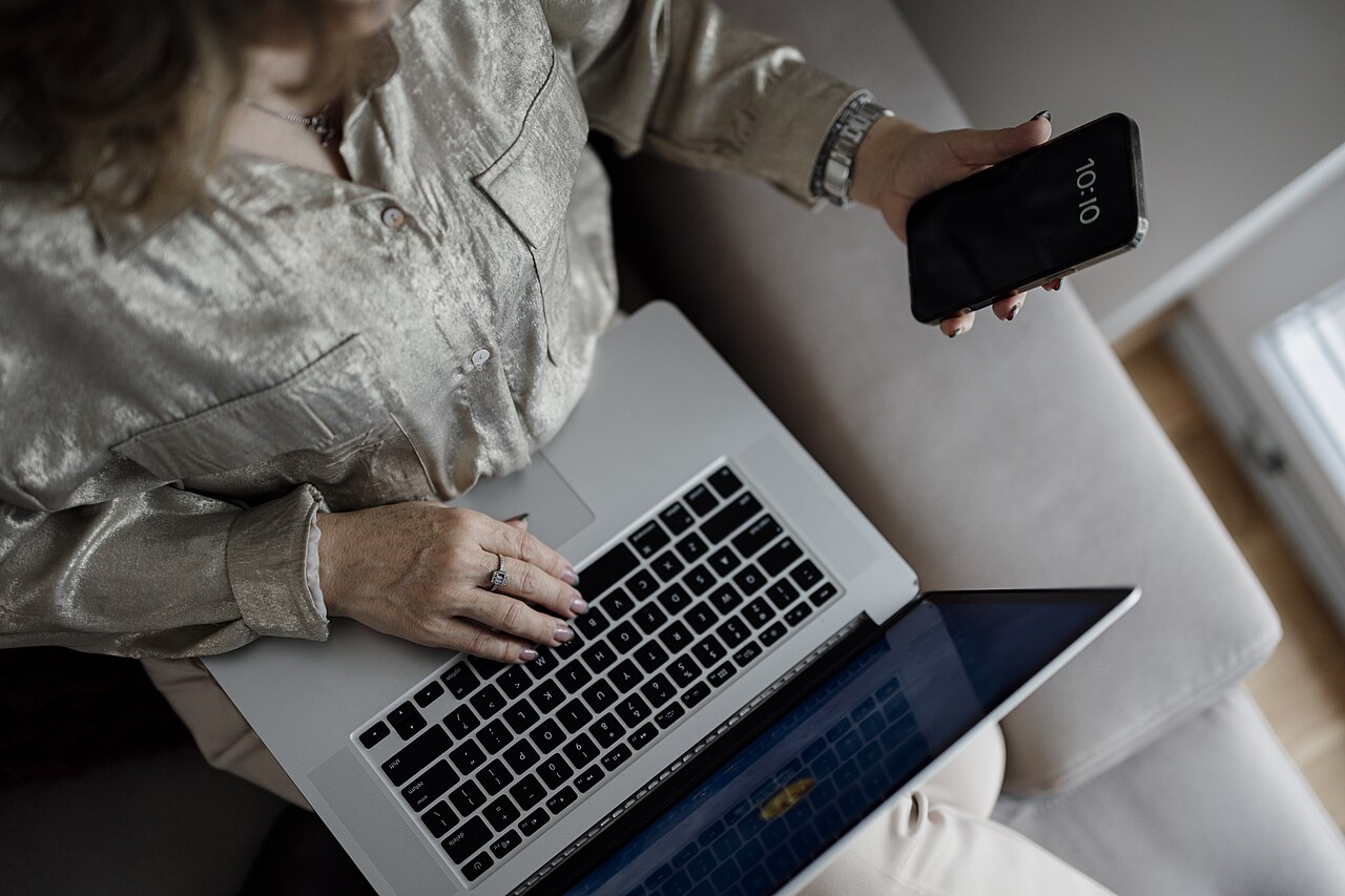 Person works on laptop while holding smartphone in living room