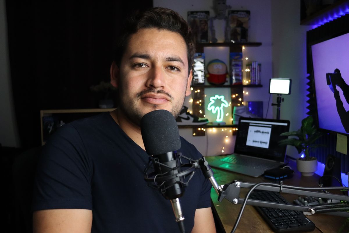A podcaster in a home studio with neon lighting and tech equipment.