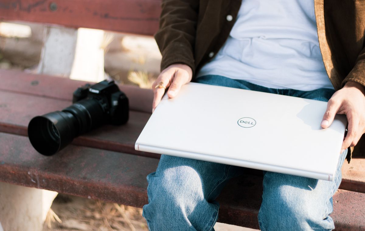 A man seated outdoors with a camera and a laptop on a bench. Perfect for creative workspace themes.