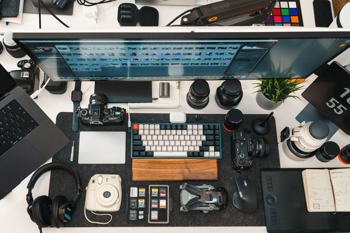 Flat lay of a photographer's organized desk setup with cameras, lens, and editing gear.