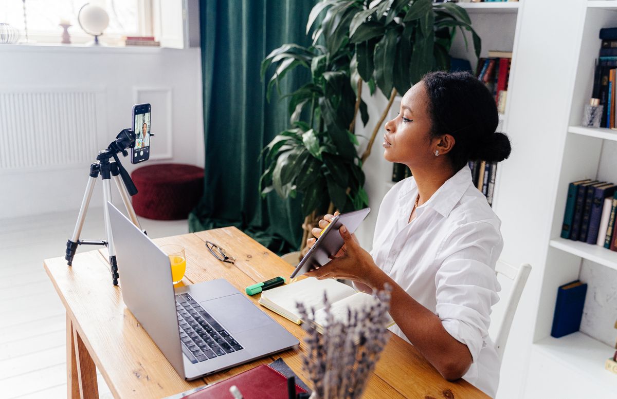 Black woman using electronic devices for vlogging indoors at home office.
