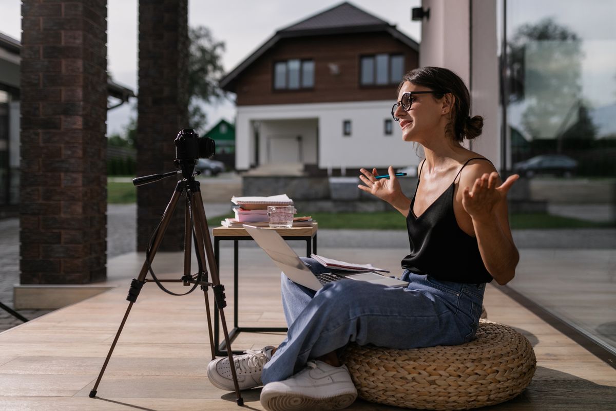 Young woman vlogging outdoors, seated with laptop and camera setup on tripod.