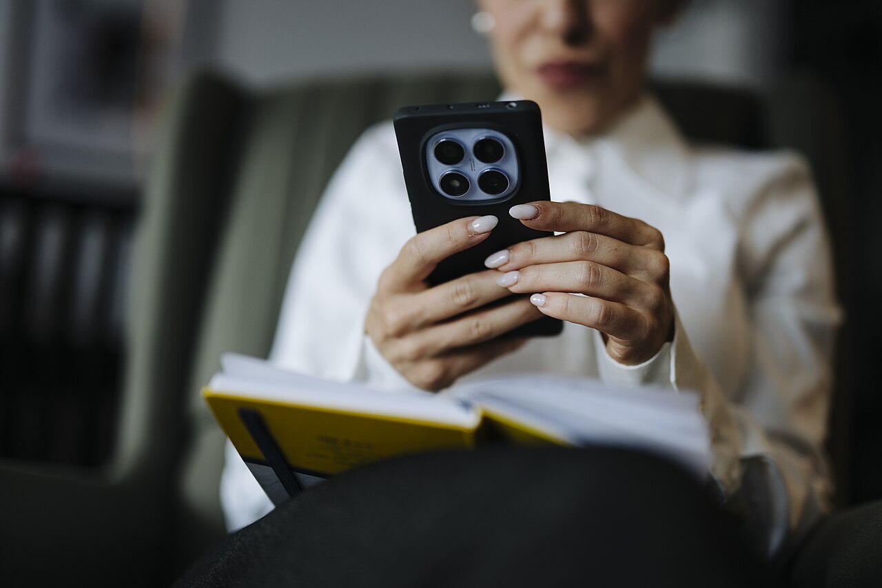 Woman sits on a chair holding a smartphone and a notebook closeup
