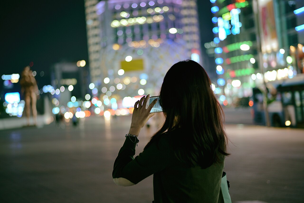 Woman taking photographs with a smartphone at night in Seoul
