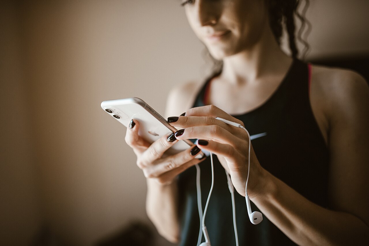 Woman using smartphone while listening to music in a fitness setting during the day
