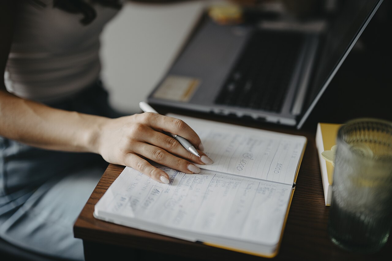 Writing notes while using a laptop at a desk